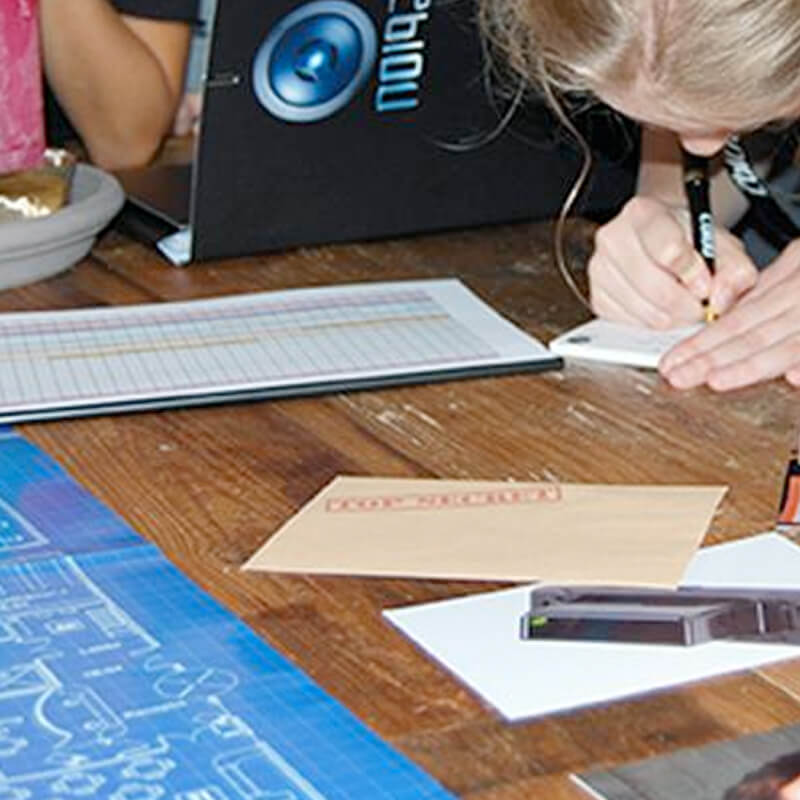 foto van kinderen binnen aan tafel die notities maken en in het misdaaddossier kijken voor een misdaadspel