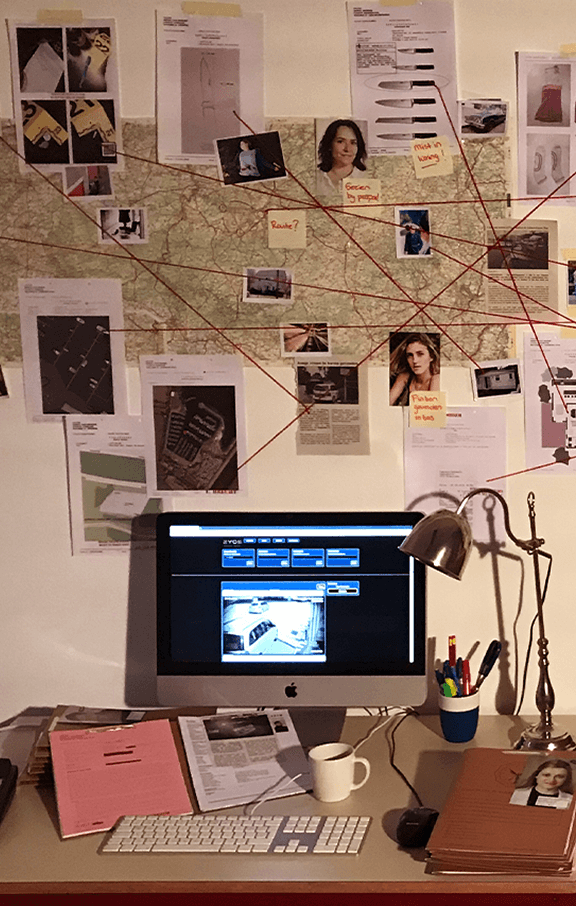 foto van een groot bewijsbord met een plattegrond, foto's, krantenartikelen en documenten met daarvoor een computer waarop bewakingsbeelden getoond worden voor een moordspel thuis